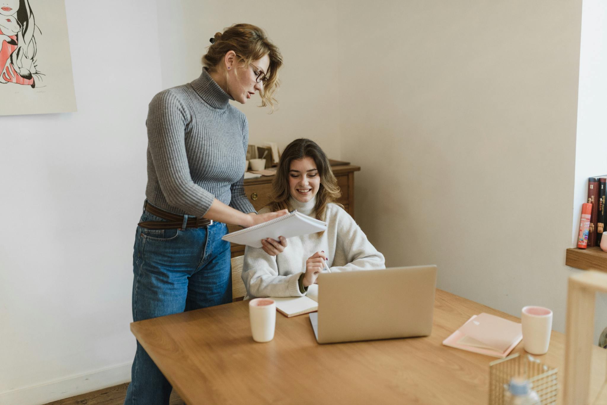 Two women collaborating enthusiastically at a desk with a laptop in a modern office.